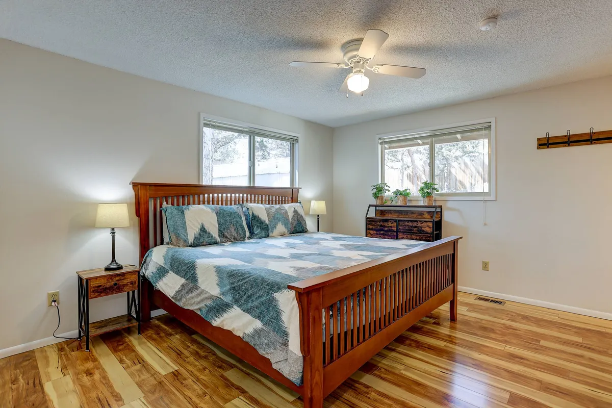 A spacious, light-filled primary bedroom featuring a plush bed with elegant linens, matching nightstands, a dressing table, and large windows that allow natural light to pour in, all contributing to a calm and restful atmosphere.