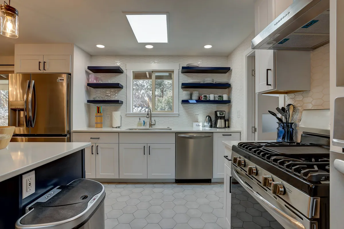 Focusing on the chef’s kitchen, this image showcases a spacious island, stainless steel appliances, hexagonal tile flooring, and open shelving. The modern kitchen setting feels homey and functional, offering ample prep and gathering space—ideal for group cooking or morning brunches.