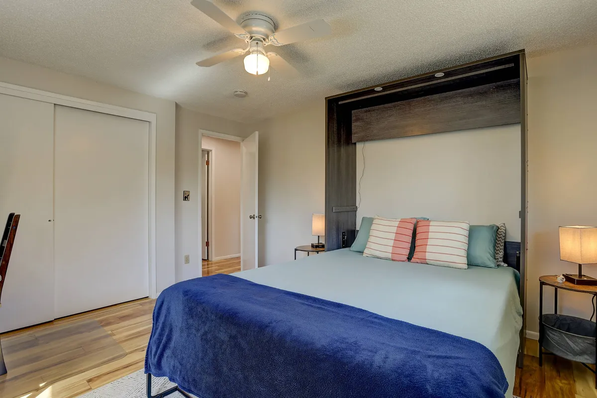 A tranquil bedroom showcasing a bed with a cozy blue throw blanket, soft-lit nightstands, and folding doors, creating an inviting space for rest or productivity.