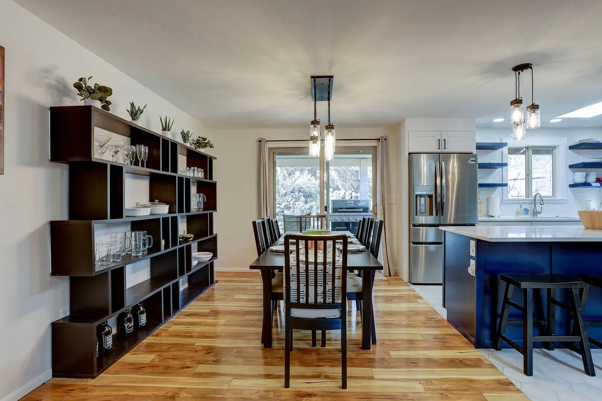 This scene highlights the dining area with a central dining table, open shelving unit, and expansive windows that flood the space with natural light. The arrangement sets the stage for family meals, festive celebrations, or heartfelt conversations in a warm, welcoming environment.