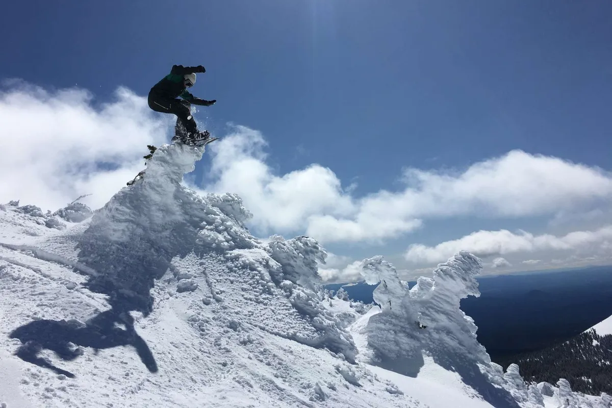 An action-packed exterior shot showing a snowboarder carving down a snow-covered peak under dramatic clouds, with wide, breathtaking mountain vistas in the background. The atmosphere is invigorating and adventurous, highlighting the outdoor possibilities nearby.