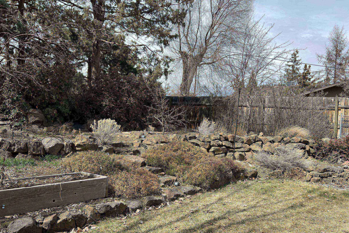 A peaceful backyard scene featuring a rock garden, raised garden bed, fence, and bare trees. The area feels private and tranquil, with ample space for relaxation or outdoor gatherings. The fenced yard suggests security for children and pets to play safely.
