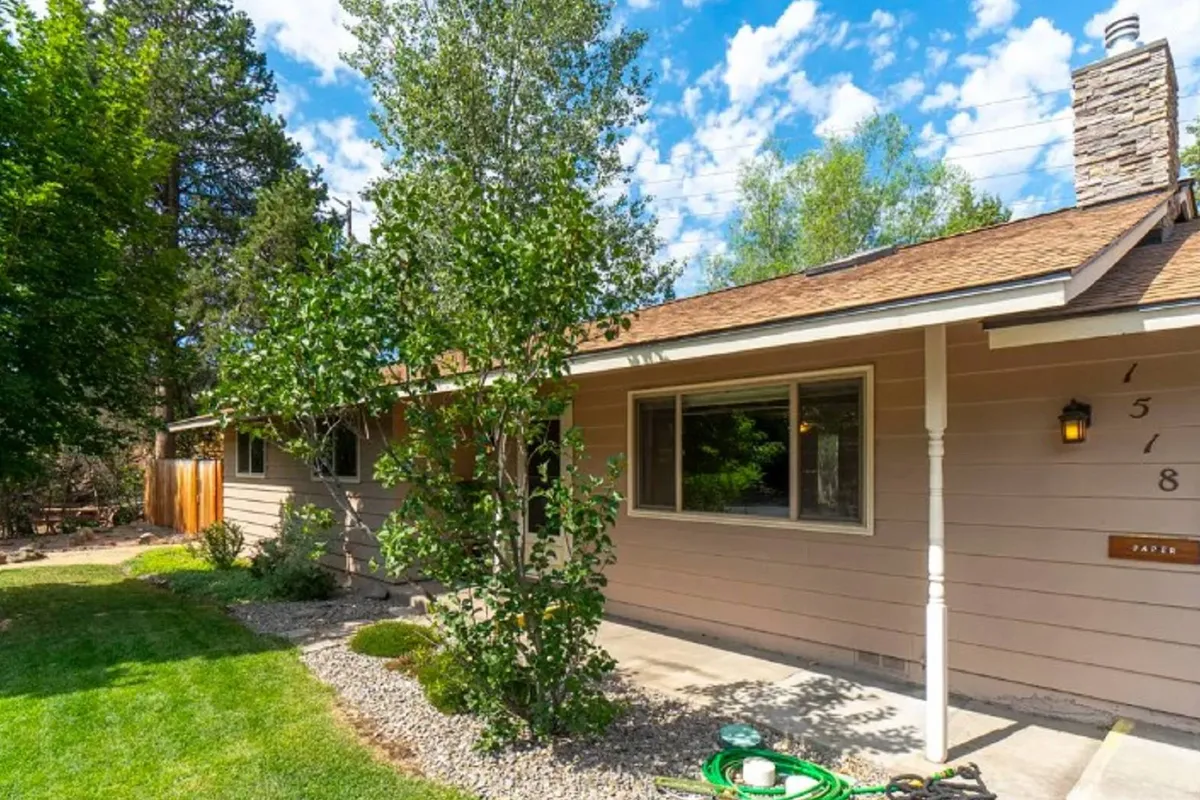 An inviting front porch surrounded by a beautifully landscaped garden, with window views and a stone chimney adding to the homey feel. The porch offers a cozy spot for relaxing outdoors or hosting small gatherings.
