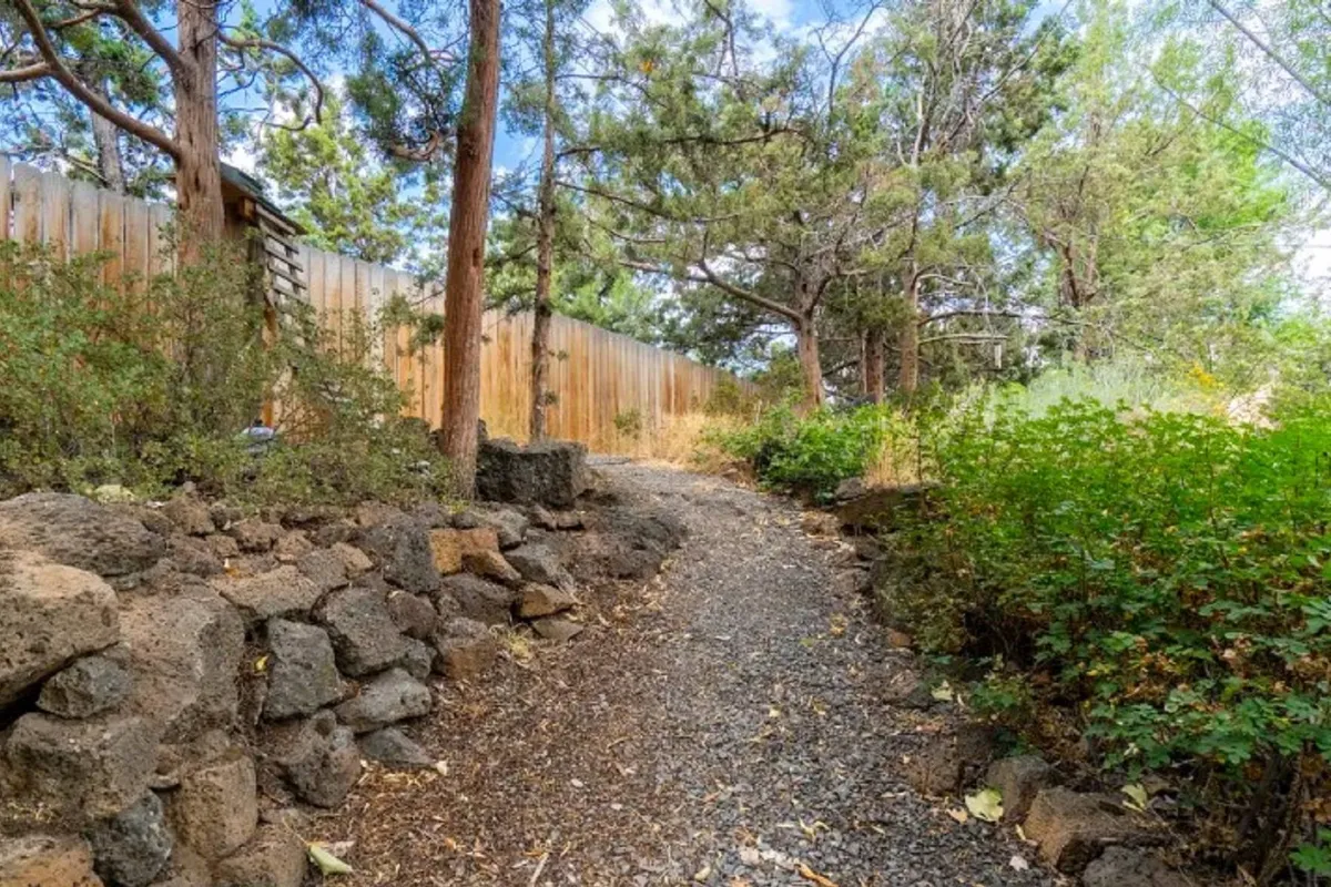 A gravel pathway winds through natural stone walls and lush greenery, offering a peaceful outdoor setting perfect for reflective walks or wildlife observation.